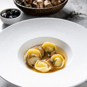 Un piatto con tortelli e brodo di funghi, con qualche funghetto a completare.